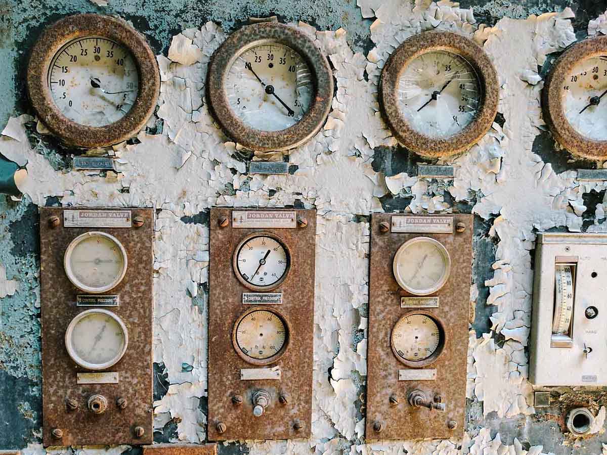 Multiple rusted dials with smashed glass faces set on a wall of peeling, flaking paint