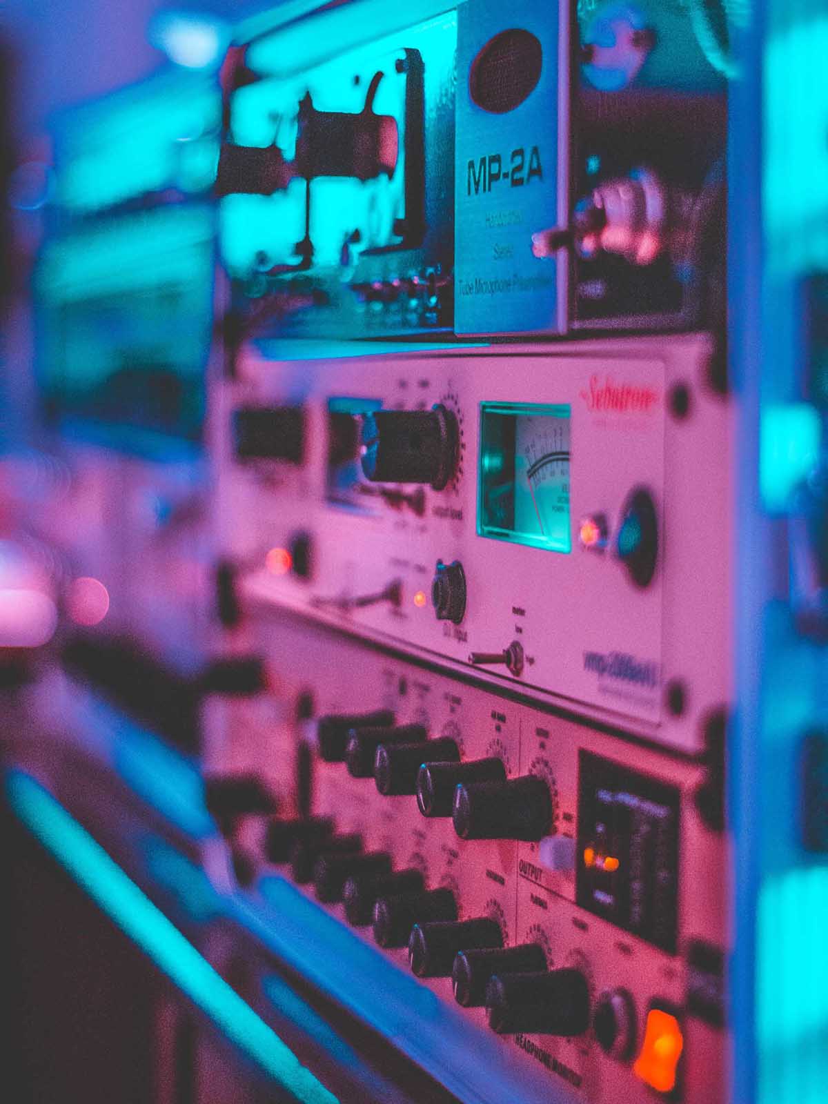 Several pieces of electrical equipment, featuring numerous dials and switches. Stacked vertically, side-lit by neon lights.
