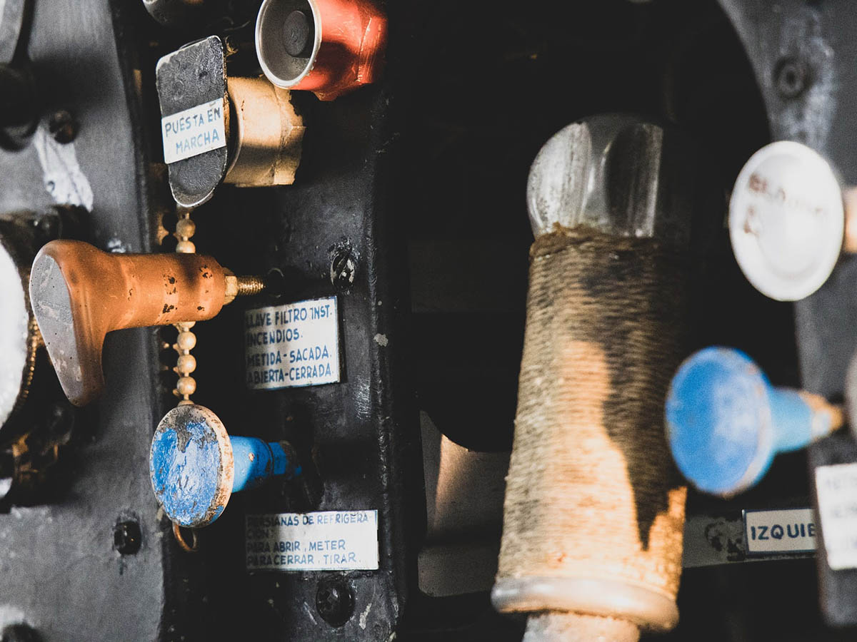 Worn looking buttons, levers and dials on metal console of a piece of machinery labelled in Spanish