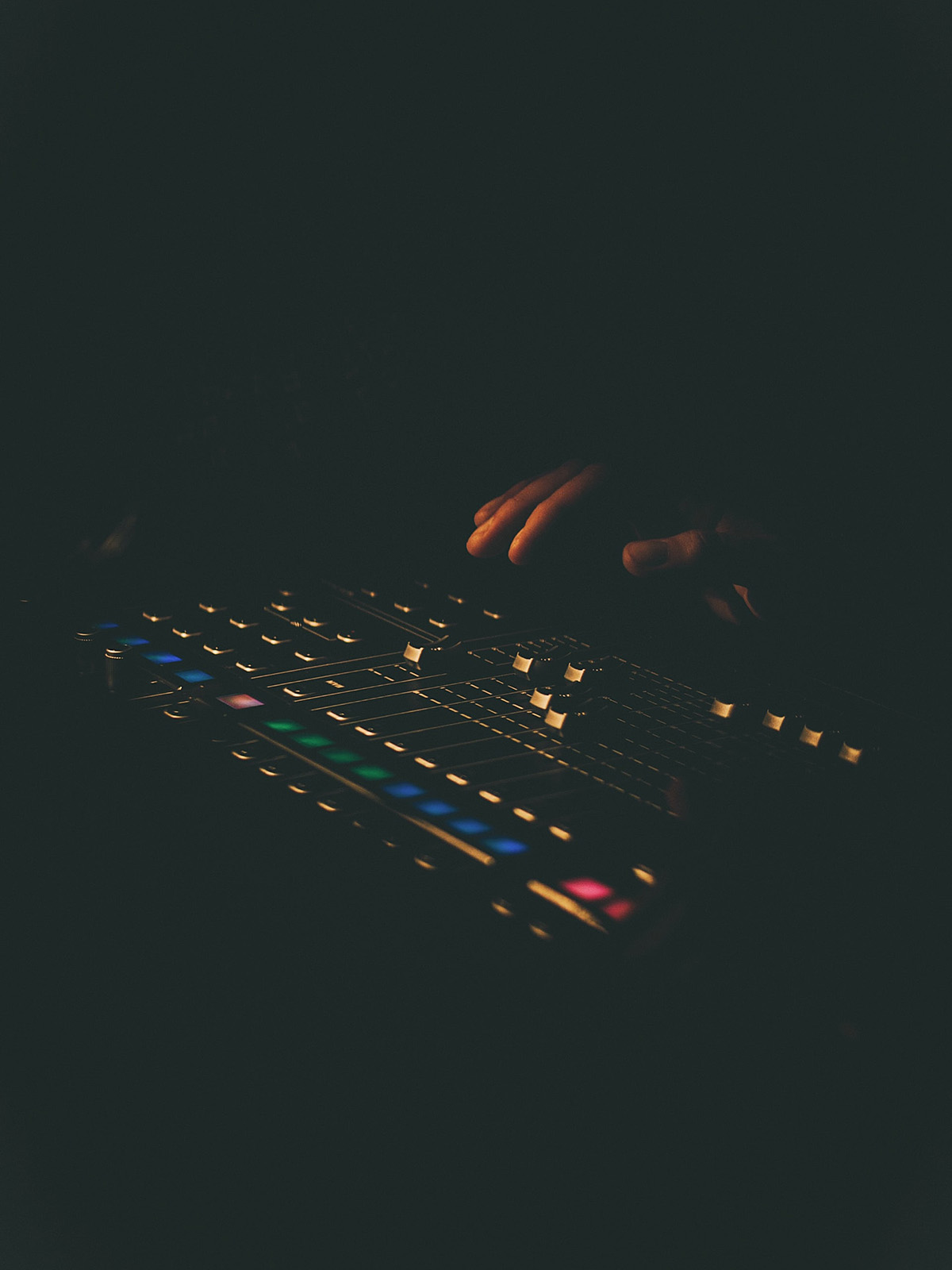Hand coming out of darkness towards sliding buttons on illuminated console