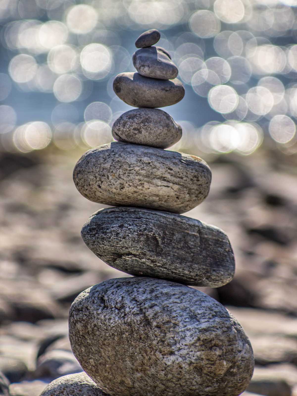 Smooth rounded river rocks balanced vertically from large to small set against sun glinting off water in background