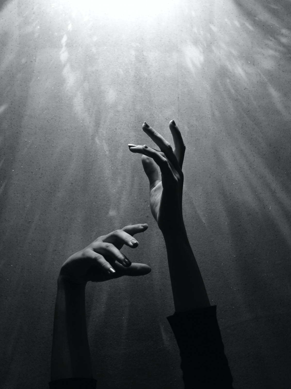Shadowy hands gracefully reaching up towards light source. Reflection on stone wall behind gives the feeling of being underwater.
