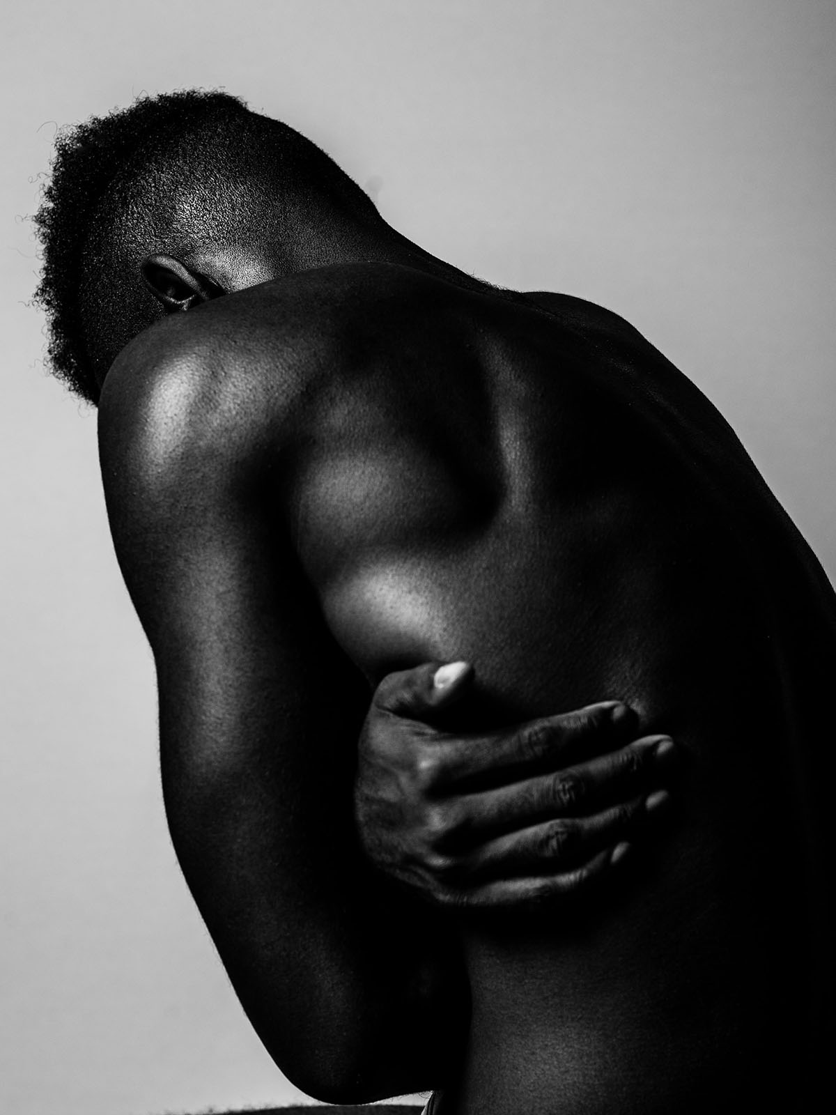 Person shown naked from waist up, facing away from camera, hugging themselves tightly. Visibly toned muscles on back and arms.