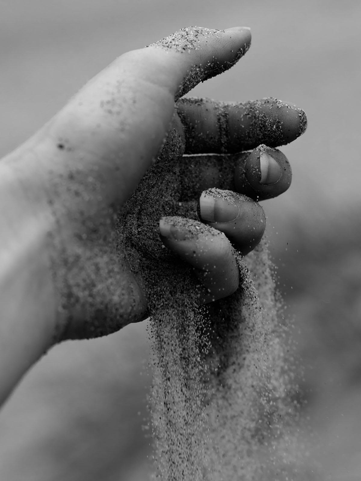 Grains of sand running through the fingers of an outstretched hand.