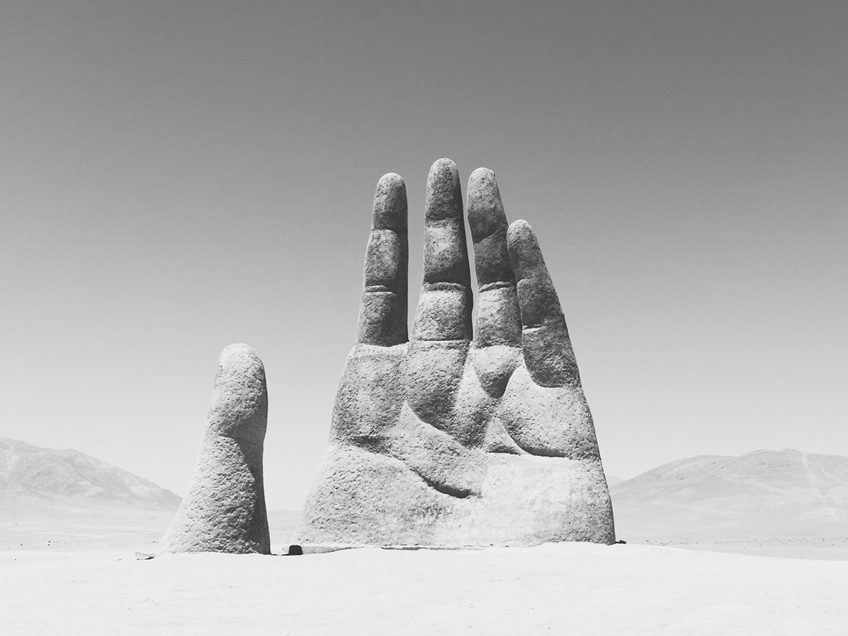 Giant stone statue of a hand rising out of an empty desert landscape.