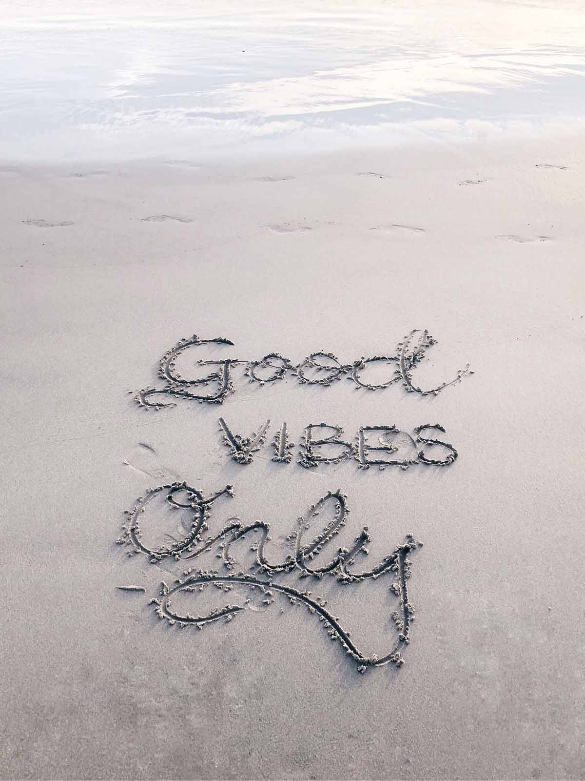 The phrase good vibes only written in wet sand at the edge of the shoreline.