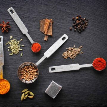 Close up stainless steel measuring spoons filled with the whole and ground spices used in my low FODMAP stock powder recipe.