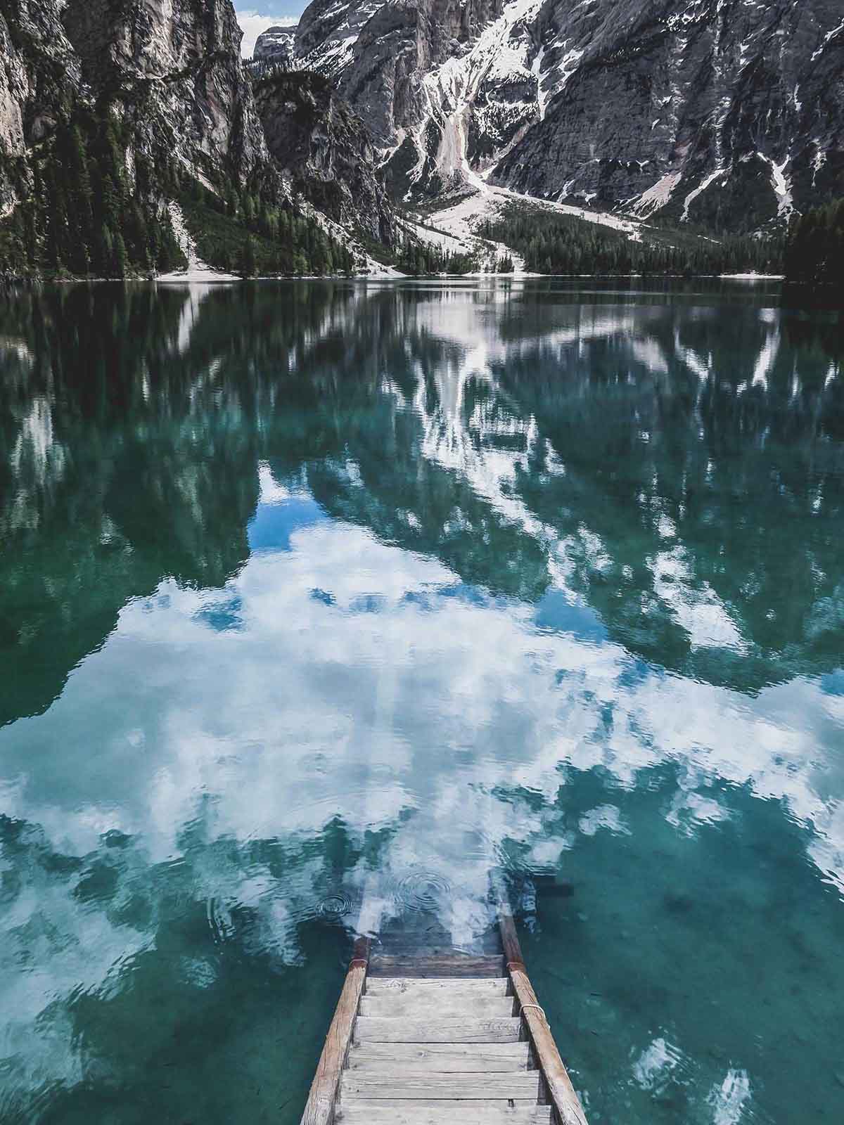 Wooden steps leading down to glacier blue tranquil lake surrounded by snow dusted mountains.