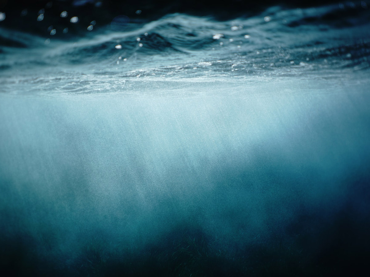 Sunlight steaking through surface of clouded blue water as seen from below.