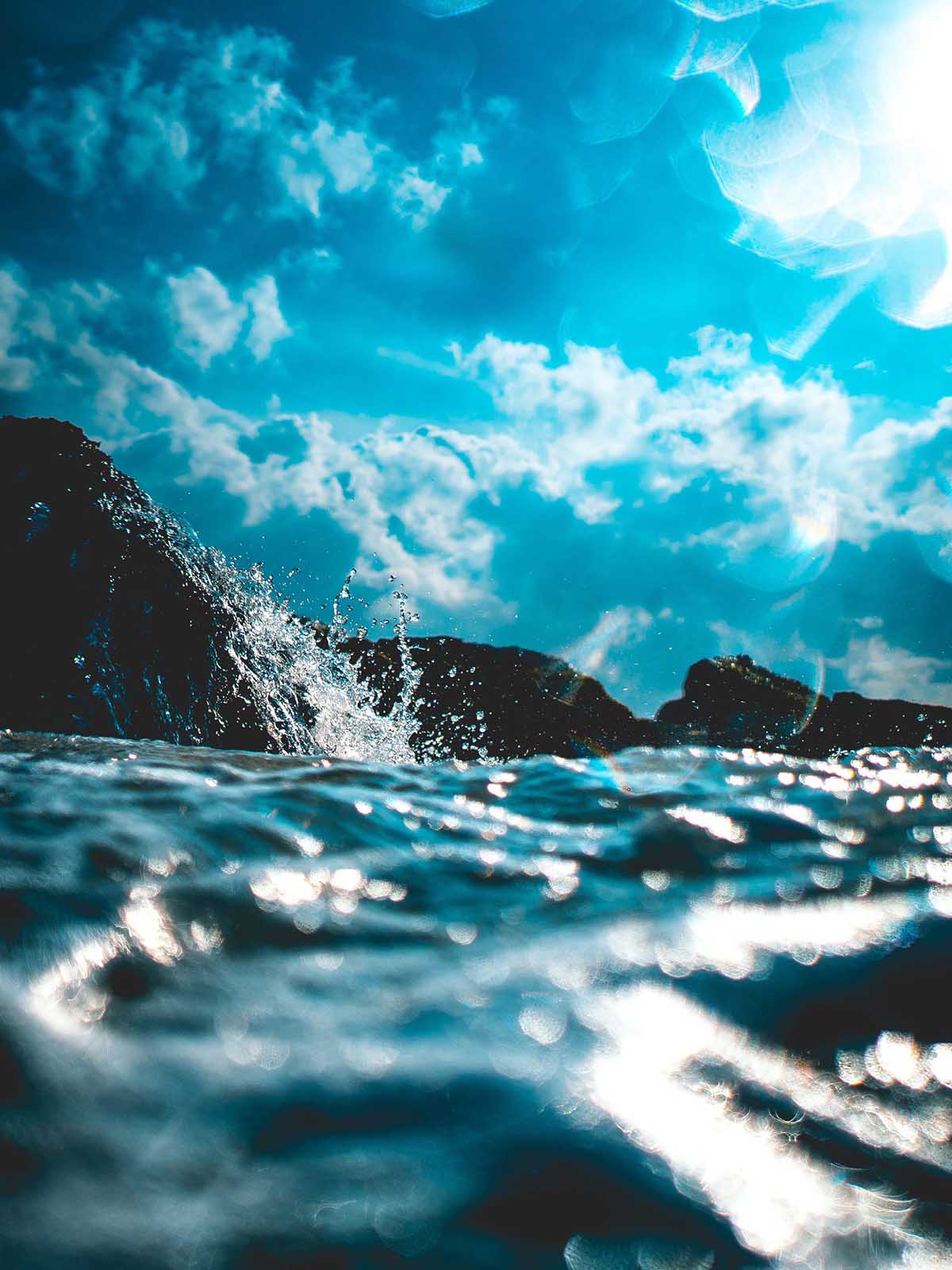 Surface of deep blue ocean as it splashes against black lava rocks.