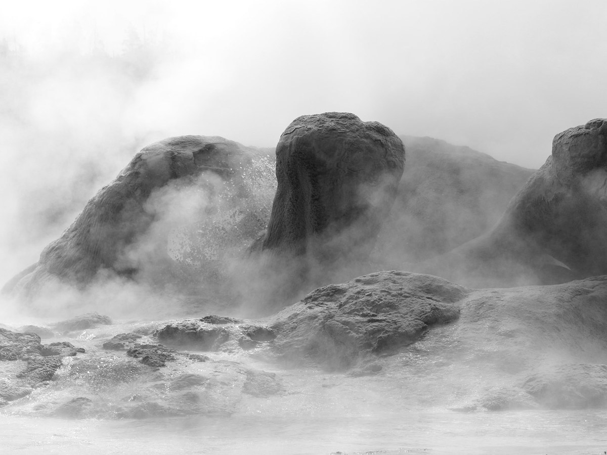 Steamy landscape as hot geyser bubbles between rocky peaks.