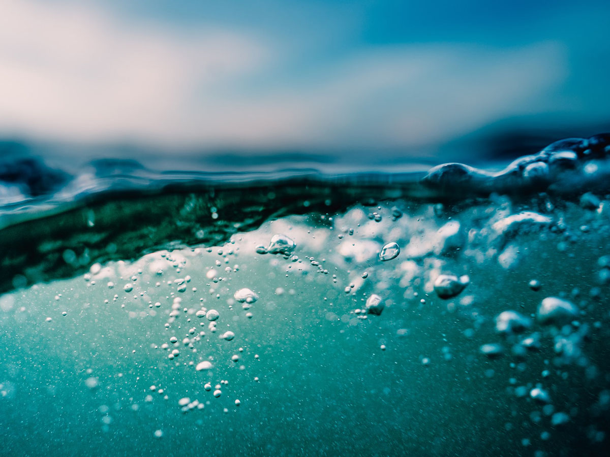 Extreme close up of rising air bubbles in blue water (presumably ocean) viewed from both above and below waterline.