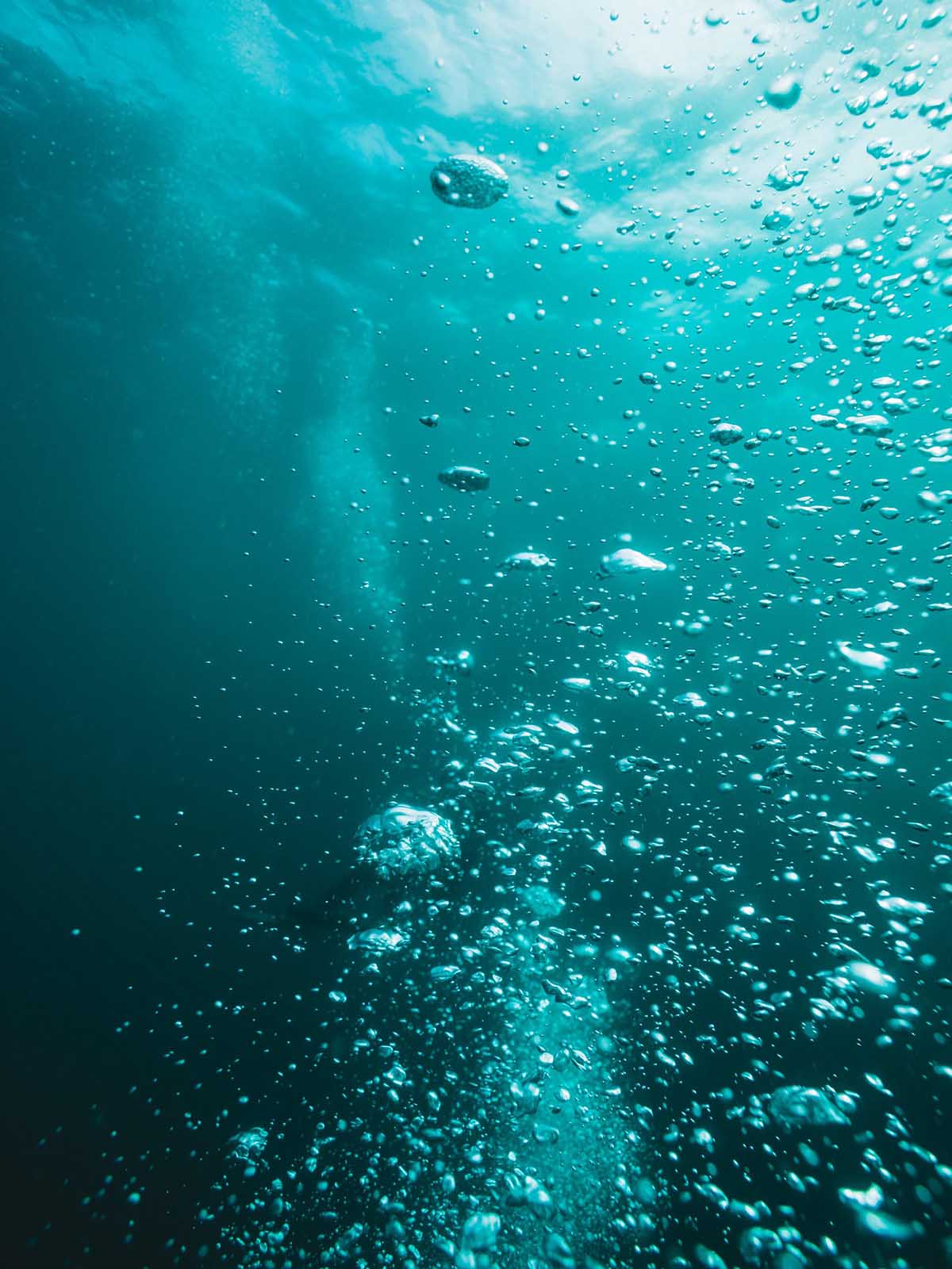 Bubbles rising in a steady stream through aqua blue water.