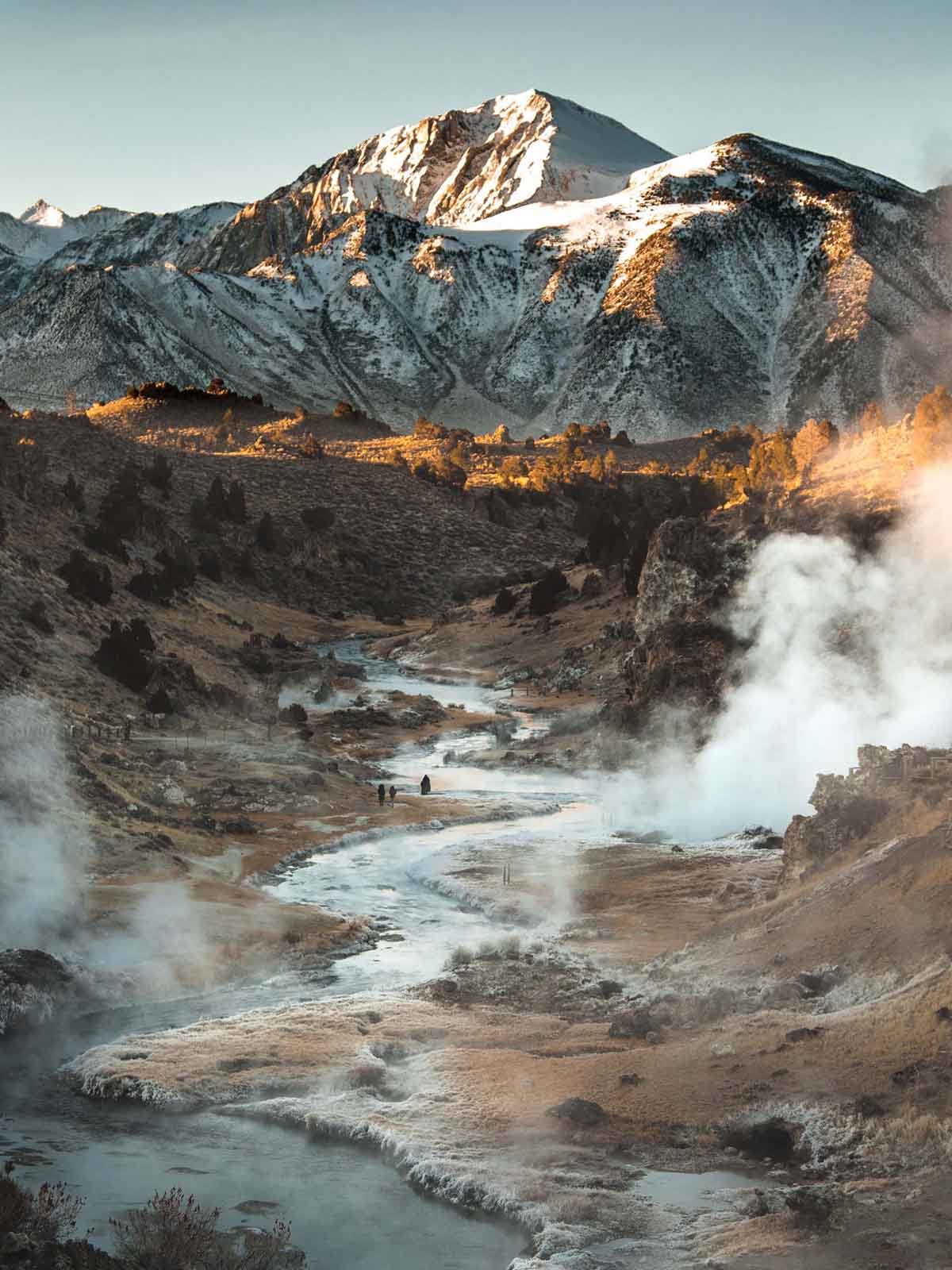 Long view across a valley of steaming hot pools to snowy distant mountains.