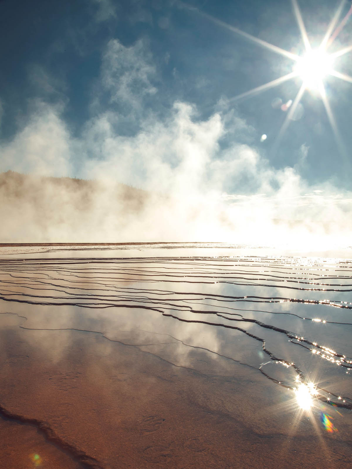 Starburst sunlight over shallow water covering layered sand flats.