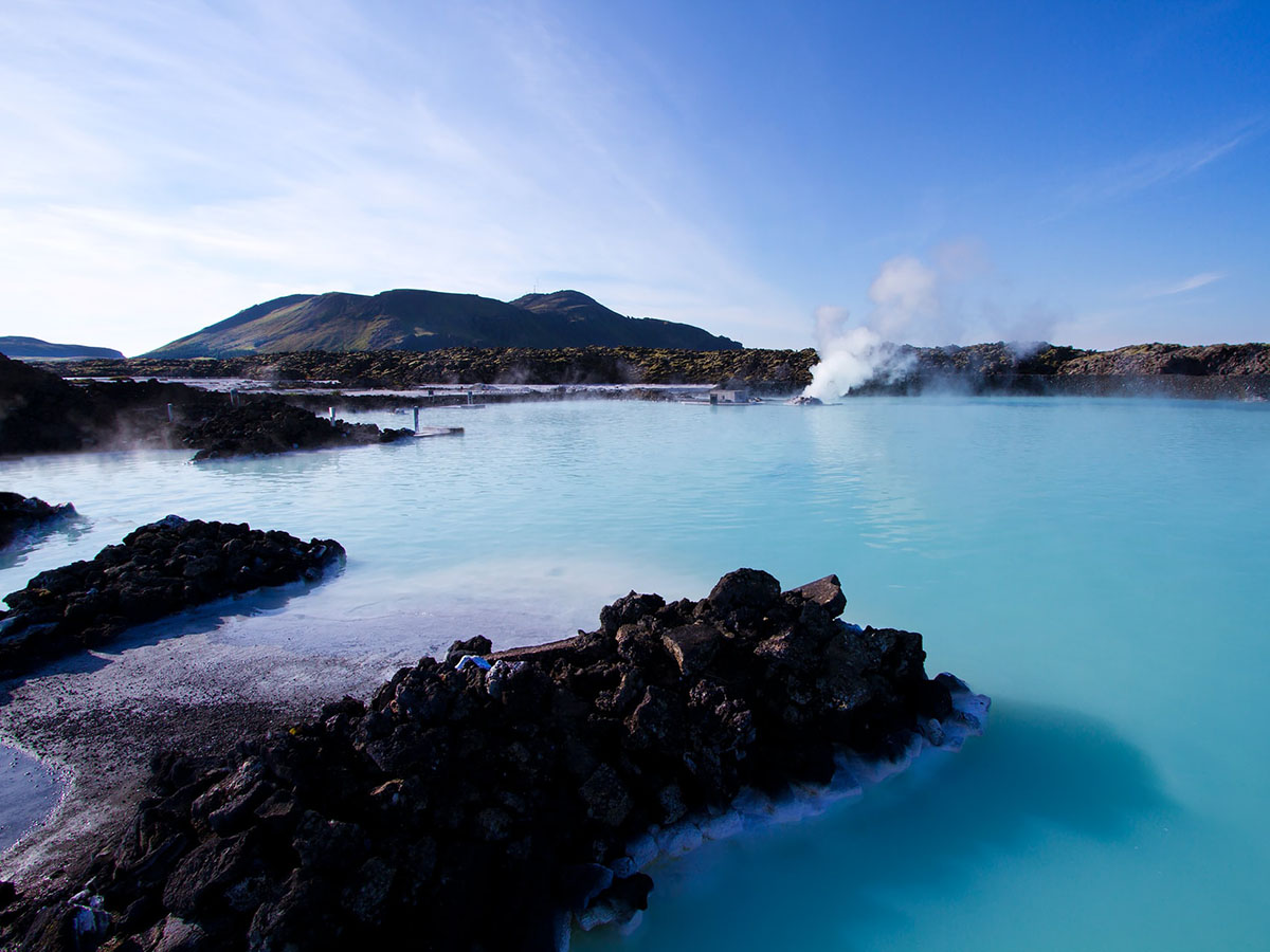 Large glacier blue pool surrounded by protruding black lava rocks.