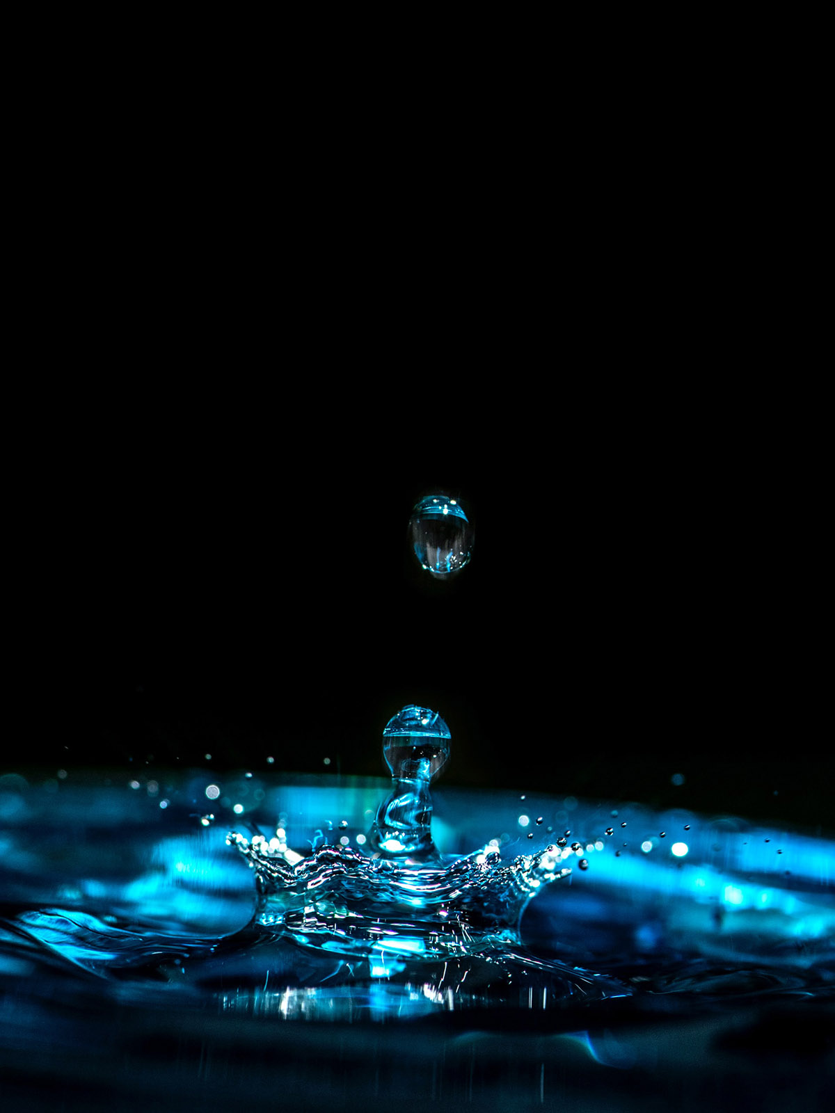 Blue water droplet frozen in motion as it splashes into water.