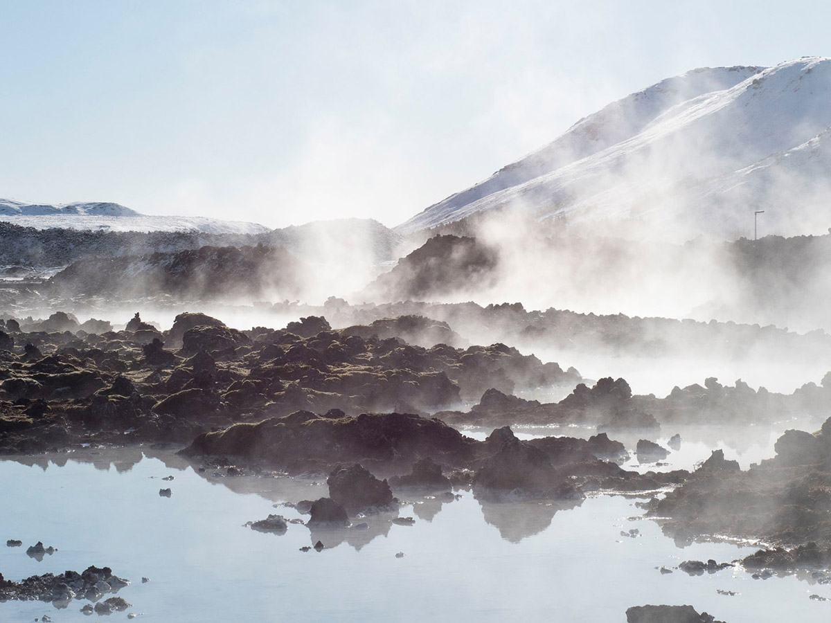 Steam rising from multiple hot pools between a landscape of lava rocks.
