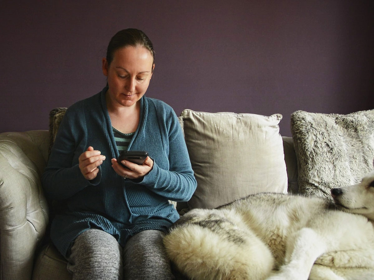 The irritable vegan she/her sitting on sofa besides her siberian husky eyes down looking at smartphone.