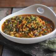 white bowl on slate tray with green vegetable soup and superfood powder in the foreground.