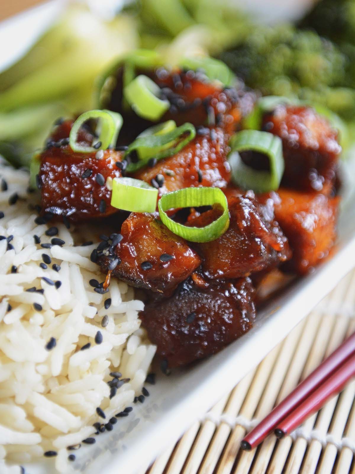 Close up of green onion and black sesame seed garnish on chunks of sticky tofu.