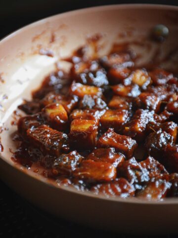 Copper pan full of sticky cubed tofu in a dark rich marinade.