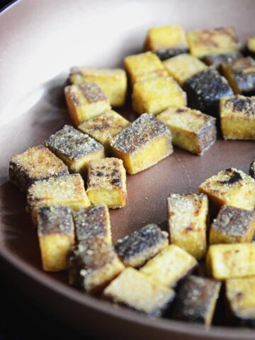 Close up of golden crispy tofu chunks frying and browning in a copper coloured pan.