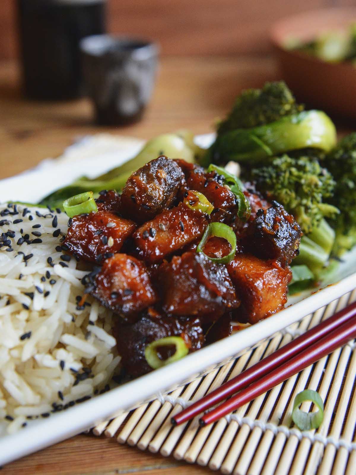 A plate of sticky, marinated tofu garnished with black sesame seeds and green onions.