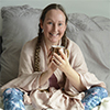 Michelle, aka the irritable vegan, a middle aged white woman that identifies by the pronouns she/her making eye contact with the camera and smiling over the top of a copper cup of creamy spiced hot chocolate.